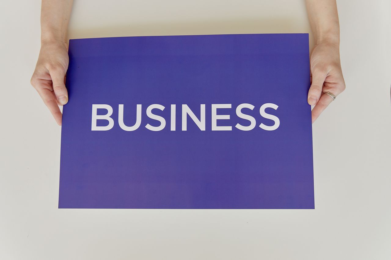 Hands holding a purple sign with the word 'BUSINESS', symbolizing corporate concepts.
